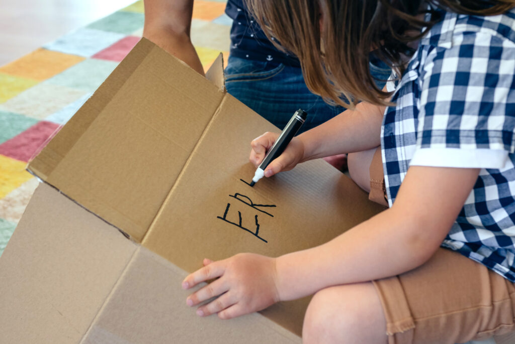 Little boy writing his name in a moving box with his father