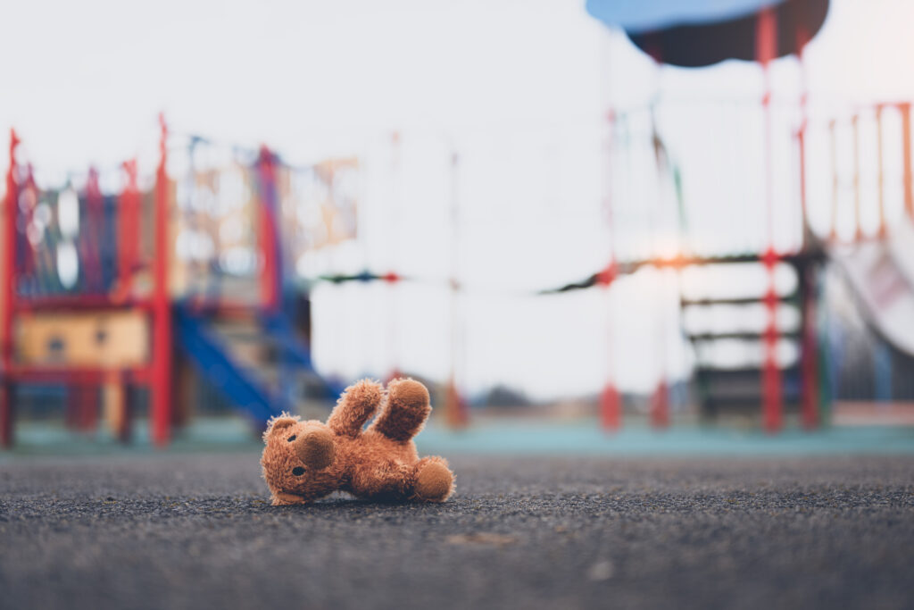 Lost teddy bear toy lying don on playground floor in gloomy day,Lonely and sad brown bear doll lied down alone in the park,lost toy or Loneliness concept,International missing Children day